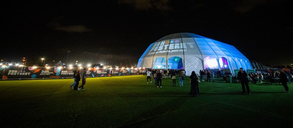 La Cúpula iluminada de azul por la noche, con gente en el césped del recinto